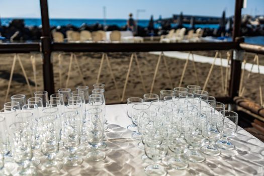 Table full of champagne and wine glasses in front of preparations for wedding party on a beach