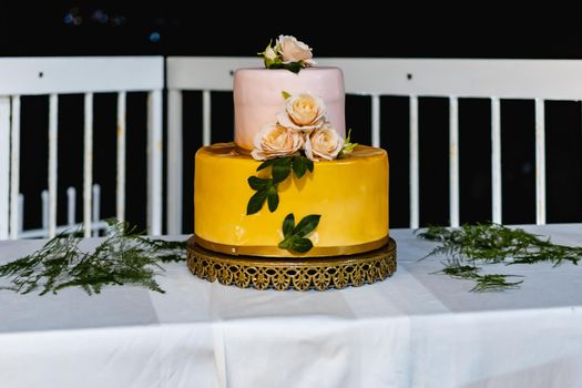 Pink and yellow wedding cake standing on table with colorful and beauty decorations around