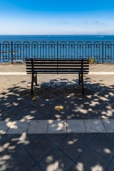 Small bench standing on the edge in front of metal railing with beautiful view to the sea