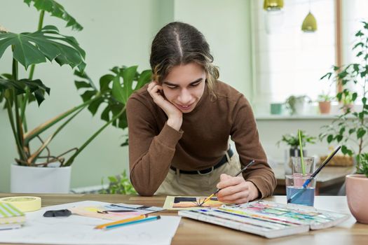 Teenager guy artist painting with watercolors at home. Creativity, adolescence, hobbies and leisure