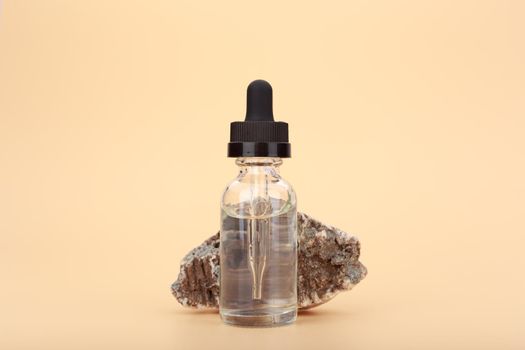 Skin serum bottle next to natural stone against bright beige background with copy space. Concept of luxury skin serum or oil for anti aging daily treatment