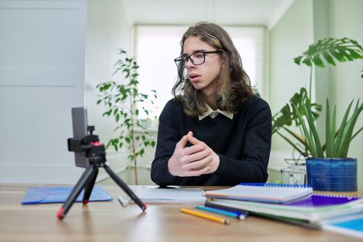 Virtual online lesson, serious teenager guy learns remotely using smartphone on tripod. Video test, meeting, e-education, technology, teaching, adolescence, distance learning, modern college school