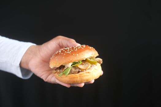 hand holding beef burger isolated on black .