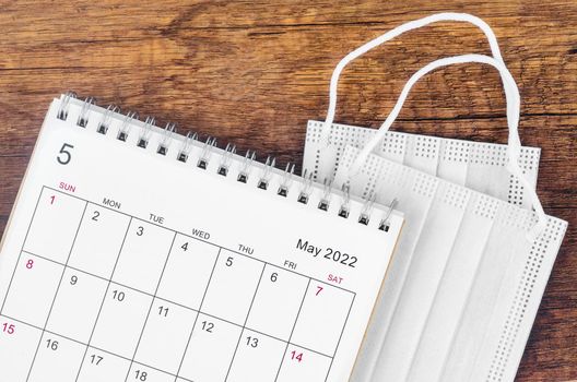 The May 2022 desk calendar with surgical mask medical on wooden background.