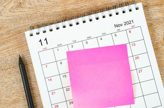 Blank sticky note on November 2021 desk calendar on wooden background for your text.