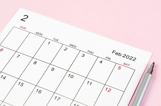 Close up February 2022 calendar sheet with pen on pink background.