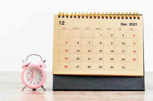 December 2021 Desk calendar with pink alarm clock on wooden table.