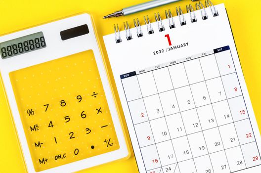 The January 2022 desk calendar with calculator and pen on yellow background.