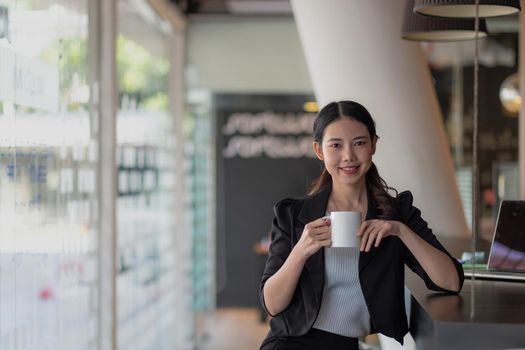 Portrait of young businesswoman smiling and looking at camera while sitting at office desk in modern office