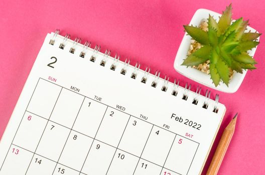 February 2022 desk calendar with pencil on pink background.