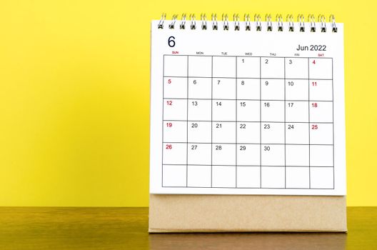 The June 2022 desk calendar with yellow background on the wooden table.
