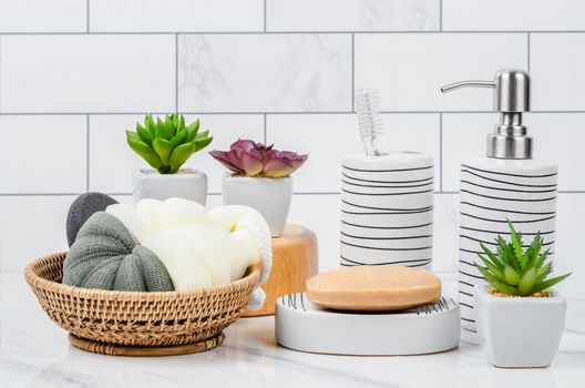 Herb soap, shower sponge and shampoo pump bottle inside a bright bathroom background.