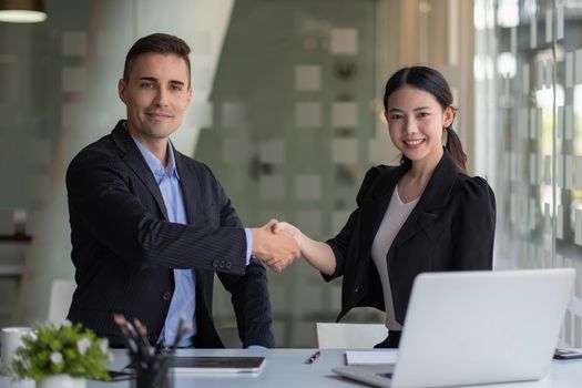 Happy caucasia male and asian female hand shaking, successful businessman handshake after good deal for both companies, business merger and acquisition concept.
