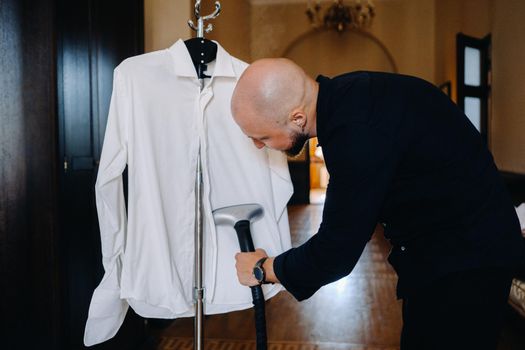 A lonely man is going to work and ironing his shirt with a steam iron.