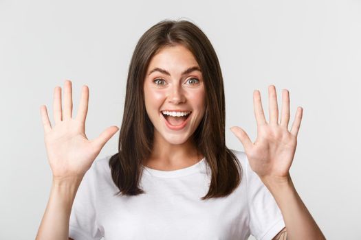 Close-up of cheerful attractive young woman smiling, showing ten fingers, white background.