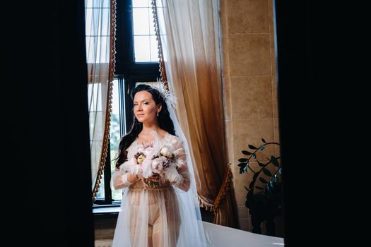 the bride, dressed in a boudoir transparent dress and underwear, sits near a vintage bath with a feather in her hands, The morning of the bride.
