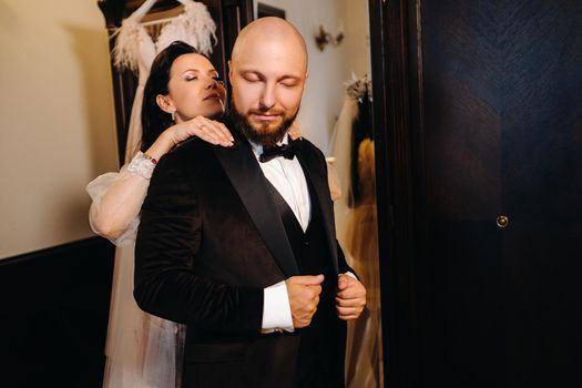 The bride in boudoir underwear dresses the groom in the interior of the hotel.