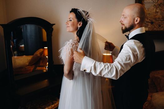 Morning of the bride. The groom helps to dress the bride in a wedding dress.