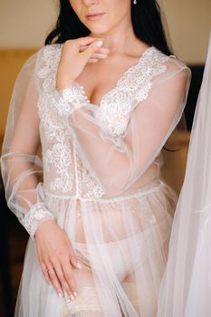 the bride, dressed in a boudoir transparent dress and underwear, stands at home in the morning.