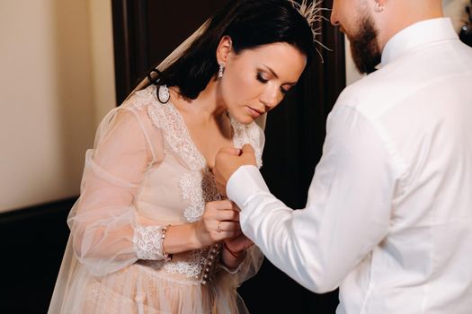 The bride in boudoir underwear dresses the groom in the interior of the hotel.