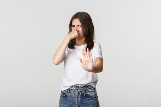 Disgusted young woman shut nose and extend hand in refusal gesture, rejecting something with awful smell.