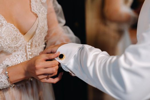 Close-up of the bride in boudoir underwear buttoning cufflinks on her sleeve