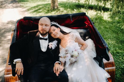 The bride and groom with a bouquet are sitting in a carriage in nature in retro style.