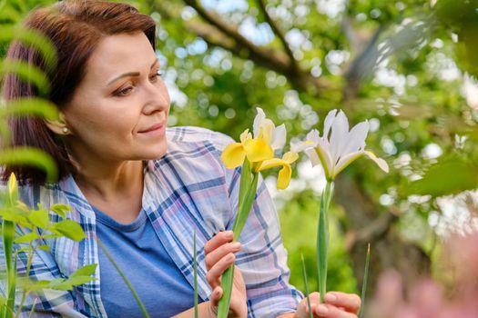 Portrait of 40s woman enjoying iris flowers in a spring garden on a flower bed. Beauty, nature, people of mature age concept