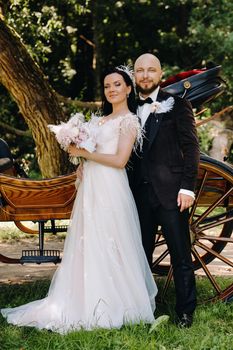 A couple of the bride and groom are standing near the carriage in nature in retro style.