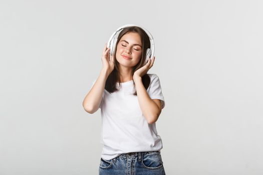 Dreamy beautiful girl enjoying listening music in wireless headphones, smiling happy.