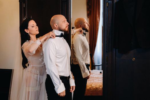 The bride in boudoir underwear dresses the groom in the interior of the hotel.