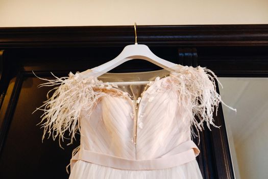 Stylish wedding dress hanging on a wooden hanger in the interior.