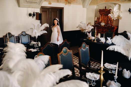 A stylish bride in a wedding dress in the interior of a restaurant decorated with feathers on the tables.