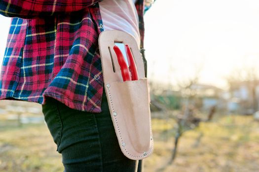 Close-up garden pruner in leather holster, case on a female gardener, spring garden background, springtime, copy space. Seasonal gardening concept