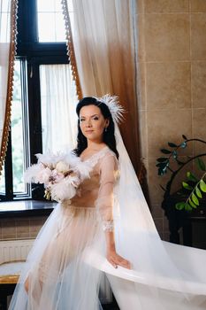 the bride, dressed in a boudoir transparent dress and underwear, sits near a vintage bath with a feather in her hands, The morning of the bride.