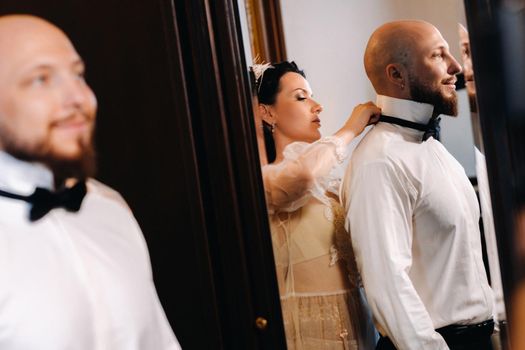 The bride in boudoir underwear dresses the groom in the interior of the hotel.