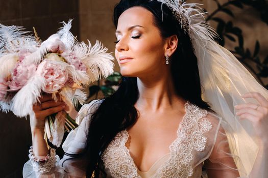 the bride, dressed in a boudoir transparent dress and underwear, sits near a vintage bath with a feather in her hands, The morning of the bride.