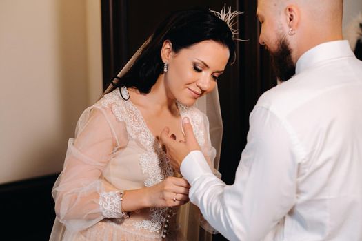 The bride in boudoir underwear dresses the groom in the interior of the hotel.