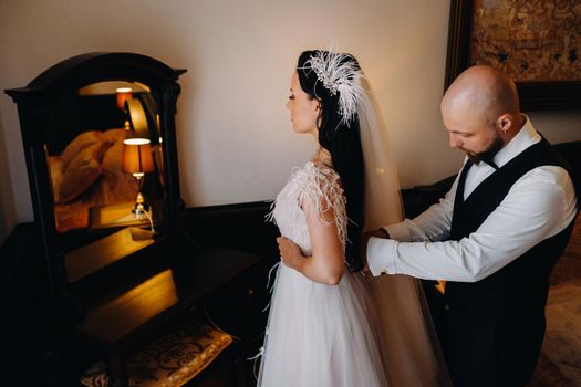 Morning of the bride. The groom helps to dress the bride in a wedding dress.