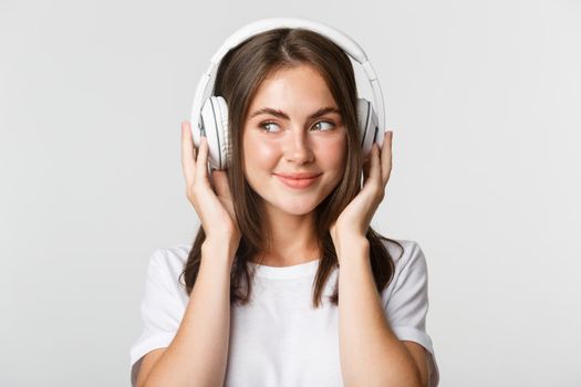 Close-up of smiling attractive brunette girl listening music in headphones, enjoying interesting podcast.