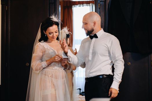 The bride in boudoir underwear dresses the groom in the interior of the hotel.