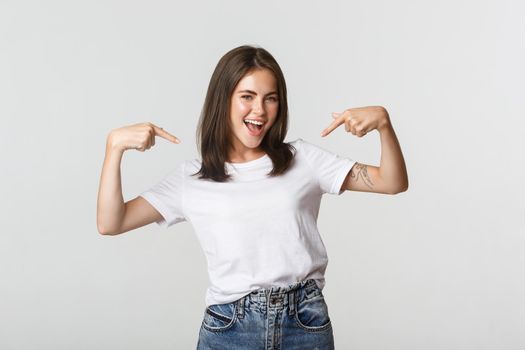 Confident attractive brunette girl smiling, pointing fingers at herself.