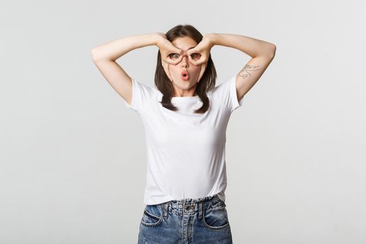 Amused cute brunette girl looking surprised and making hand glasses gesture.