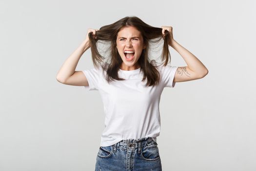 Outraged mad young woman ripping hair on head and yelling angry.
