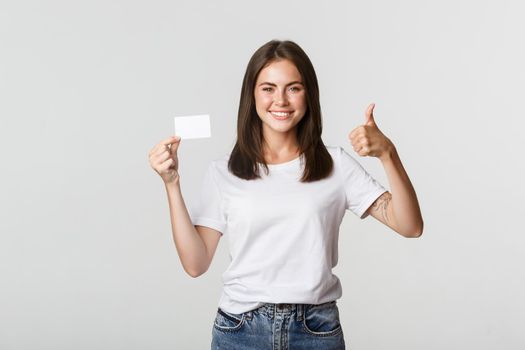 Satisfied attractive girl showing credit card and thumbs-up.