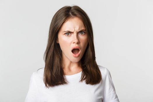 Close-up of outraged insulted young woman looking frustrated and frowning, white background.