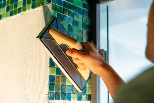 Construction worker installing ceramic mosaic boards on flexible adhesive.