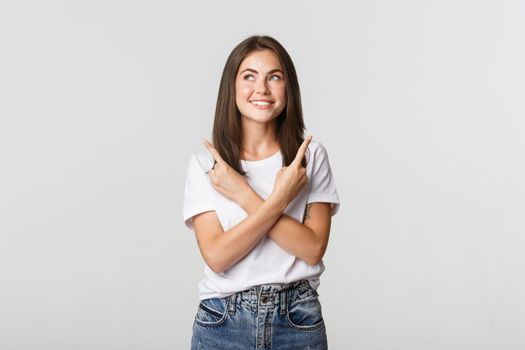 Thoughtful smiling woman looking upper left corner pleased, pointing fingers sideways.