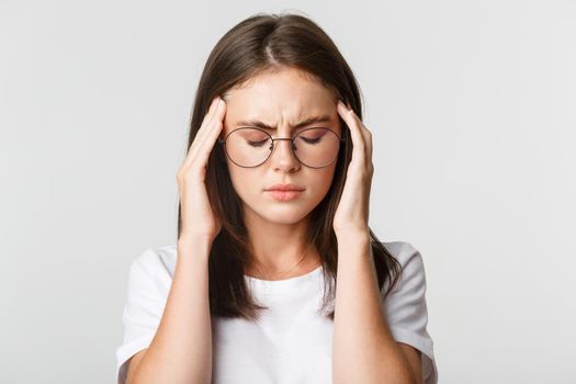 Close-up of young woman in glasses touching head and grimacing from pain, having headache or migraine, feeling sick.