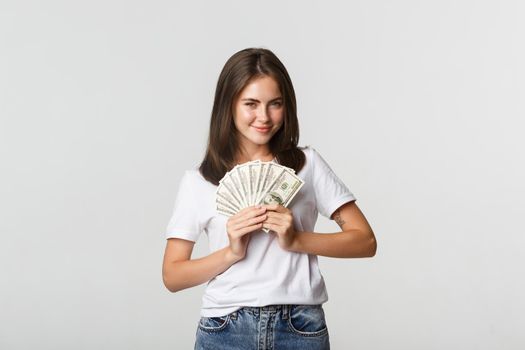 Greedy smiling girl looking cunning and holding money, standing white background.